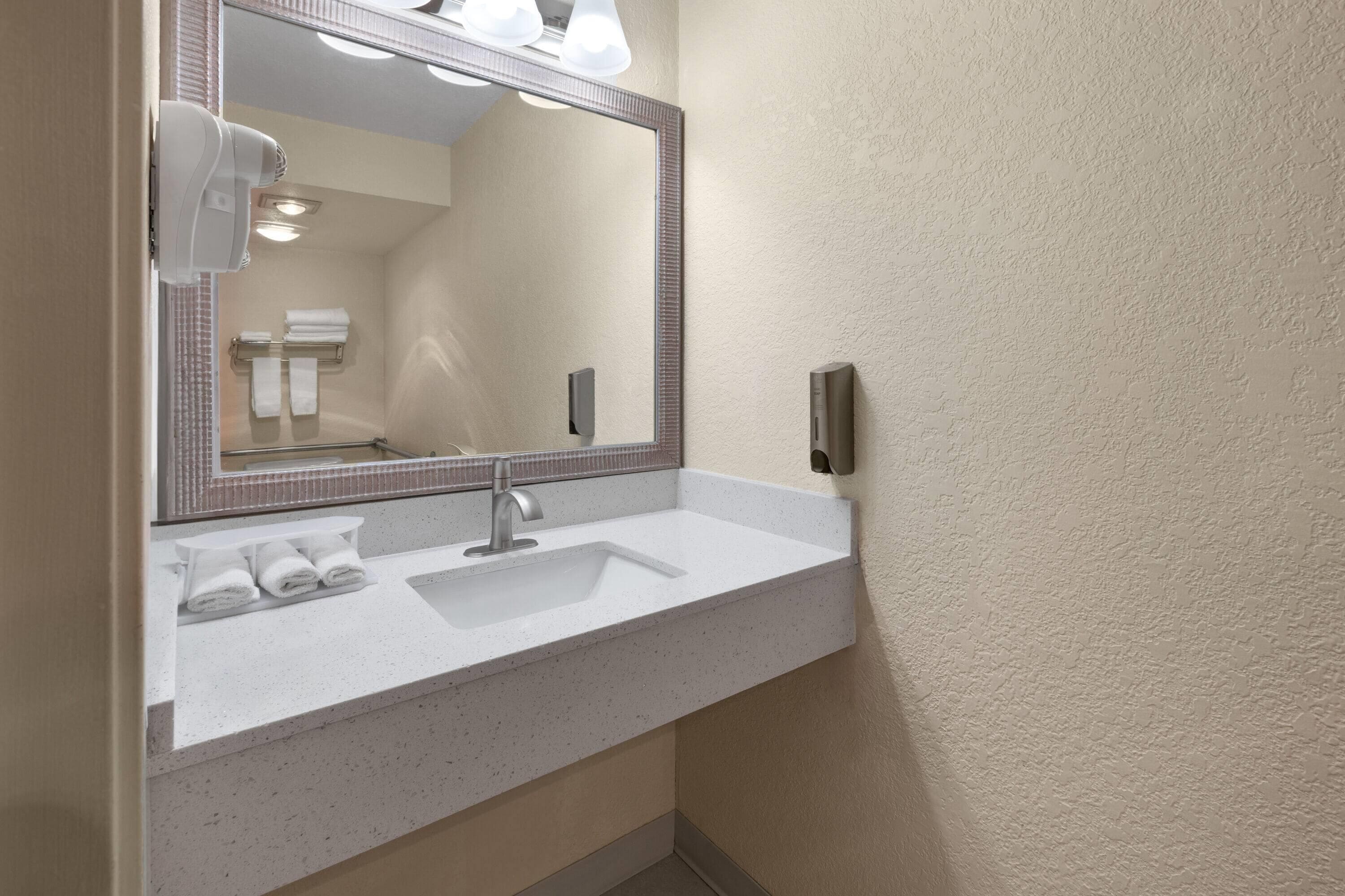 A bathroom with a white sink, a large mirror, and a towel rack with towels.