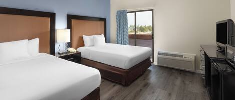 A hotel room with two beds, a television, a desk, and a window with a view.