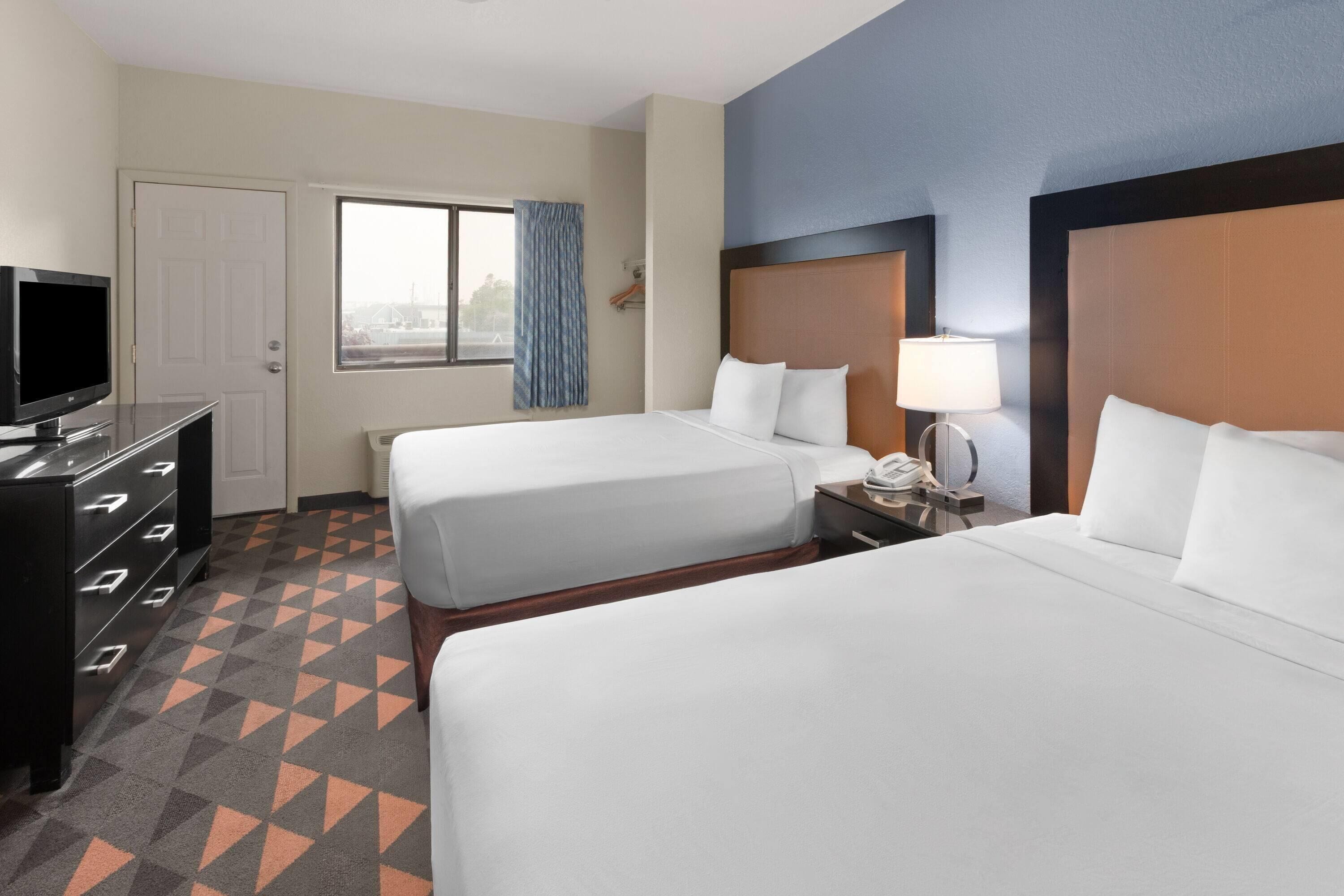 A hotel room with two beds, a TV, a desk, and a window with curtains.