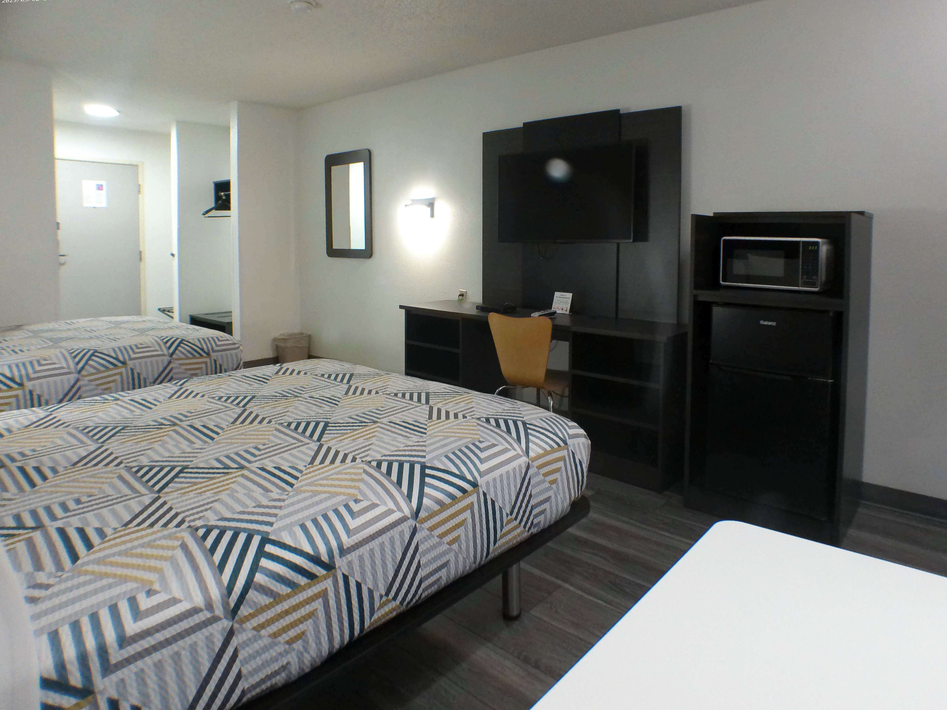 A hotel room with a bed, a desk, a chair, a television, and a microwave.
