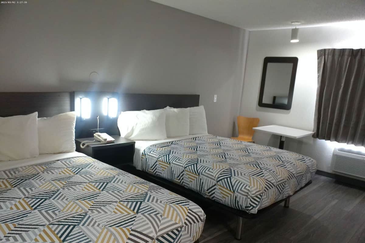 A hotel room with two beds, a desk, a chair, a phone, and a mirror.