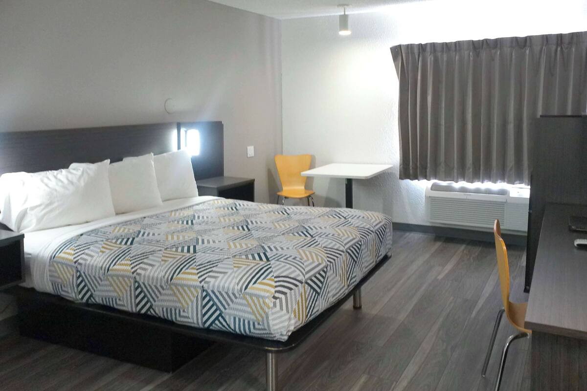 A hotel room with a bed, a desk, a chair, and a window with curtains.