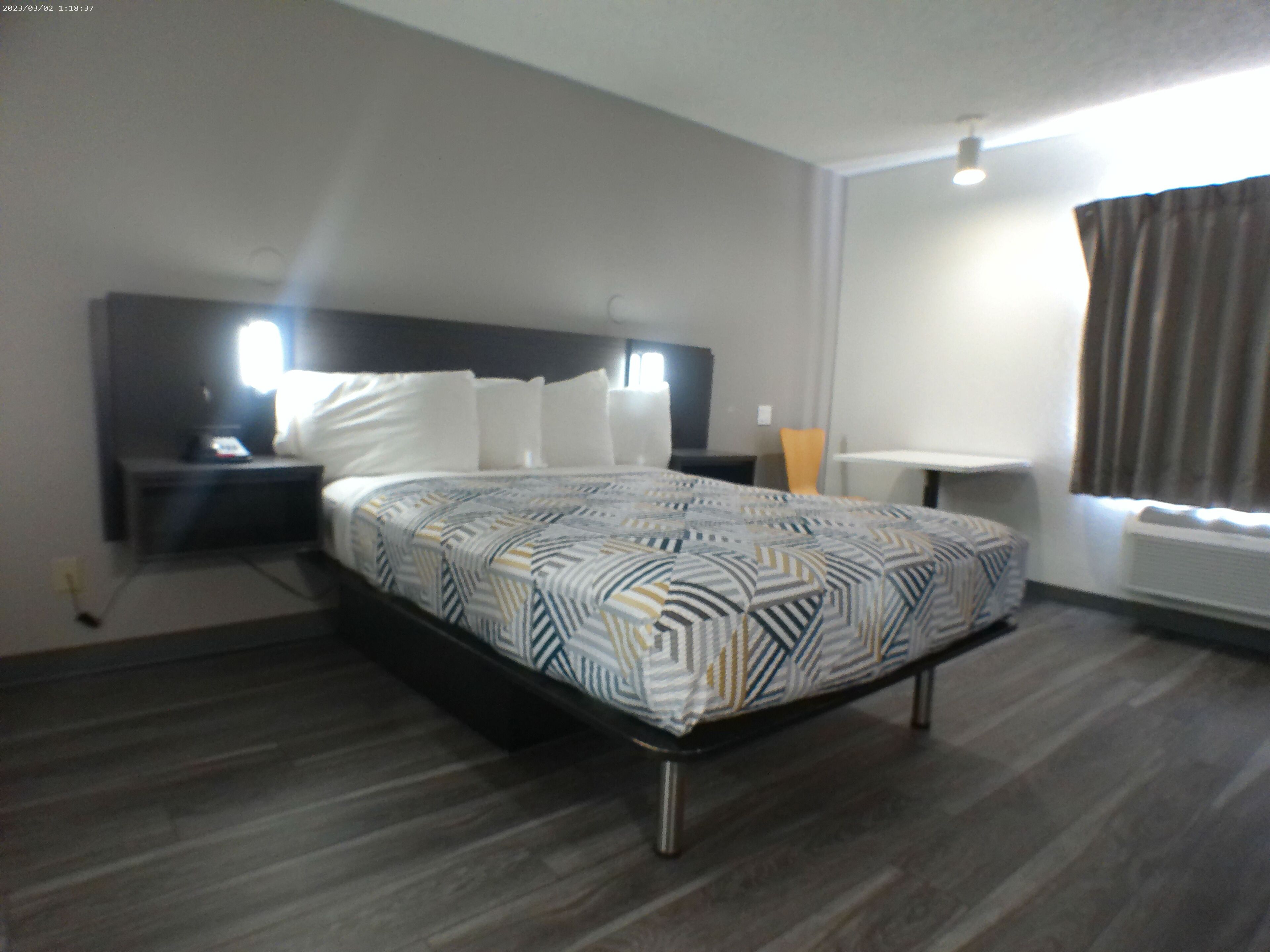 Une chambre d’hôtel avec un lit, des tables de chevet, un bureau et une fenêtre avec des rideaux.