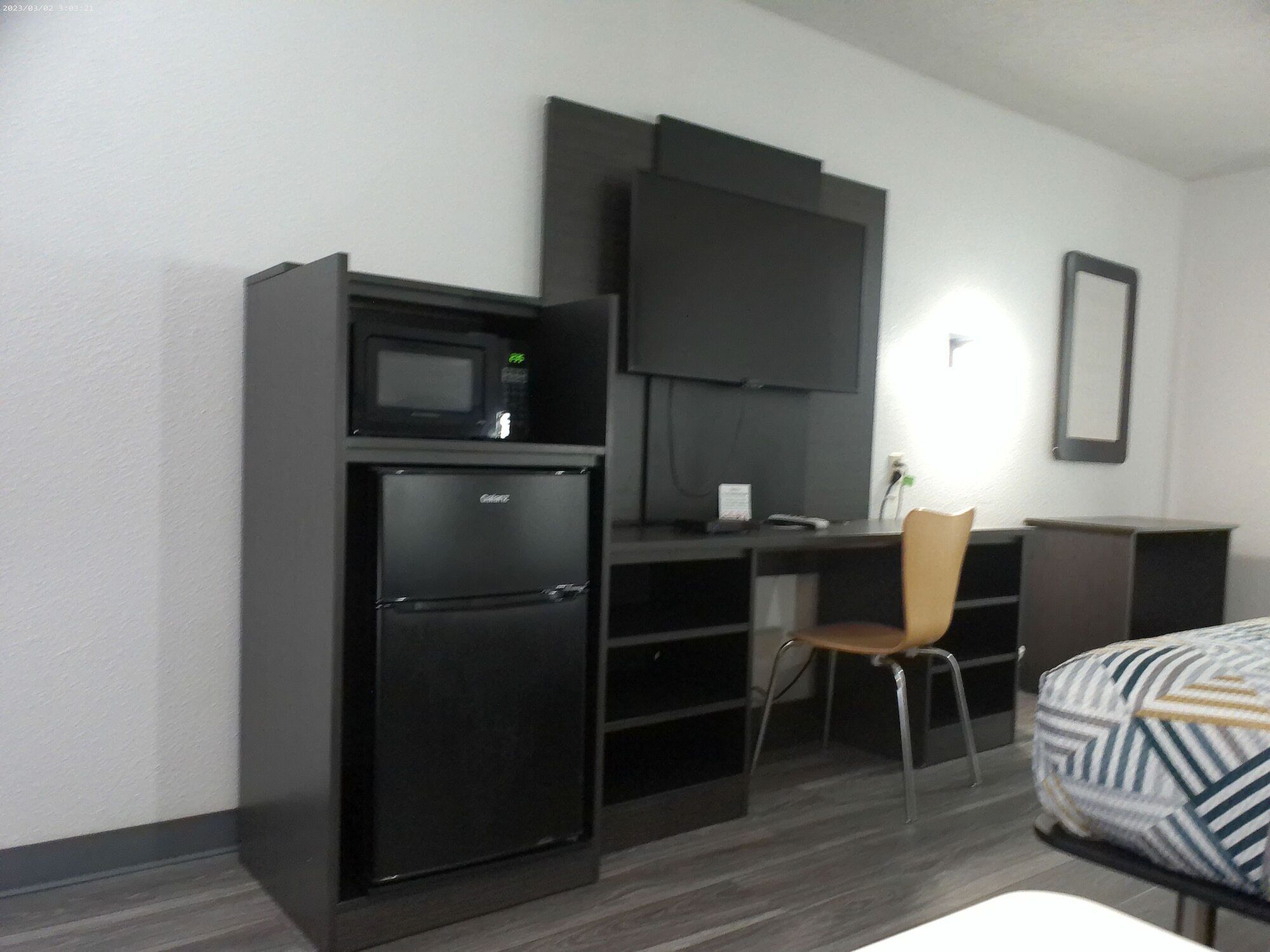 A compact hotel room with a kitchenette, a flat-screen TV, a single bed, and a chair.