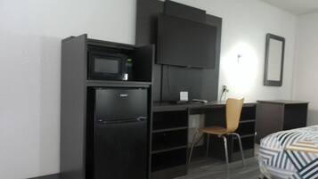 A compact hotel room with a kitchenette, a flat-screen TV, a single bed, and a chair.