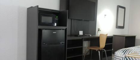 A compact hotel room with a kitchenette, a flat-screen TV, a single bed, and a chair.