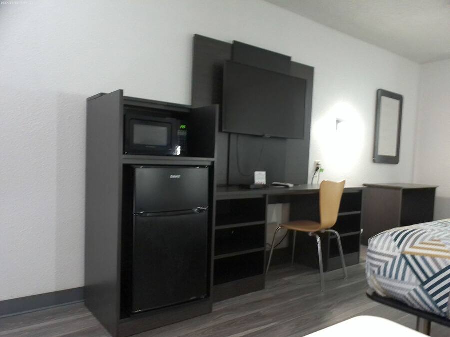 A compact hotel room with a kitchenette, a flat-screen TV, a single bed, and a chair.