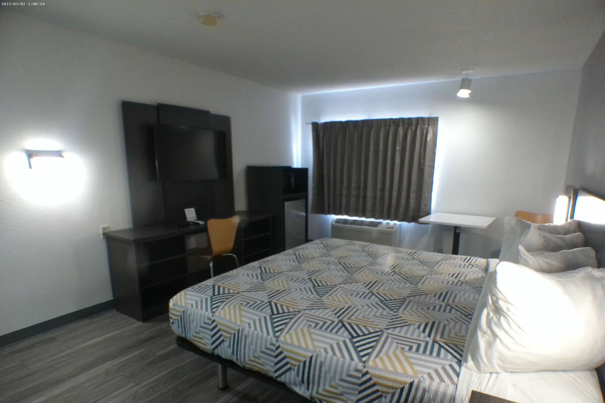 A hotel room with a bed, a desk, a chair, a television, and a window with curtains.