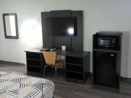 Una habitación con cama, escritorio, silla, televisor y microondas.