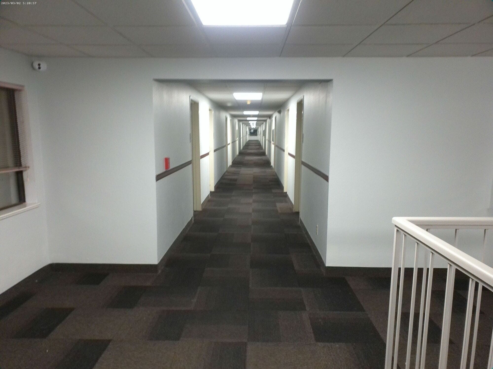 A long, narrow hallway with white walls and a checkered carpet.