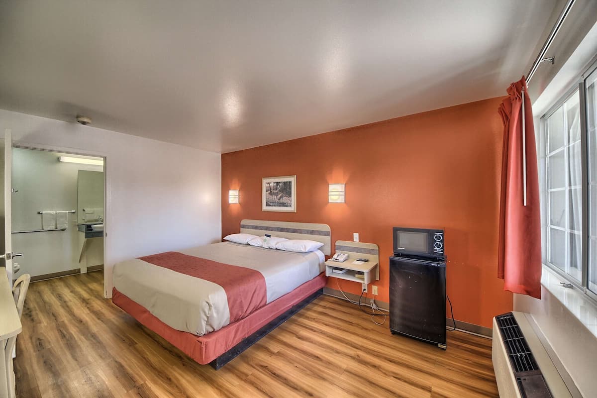 A hotel room with a bed, bedside table, TV, and a heater.