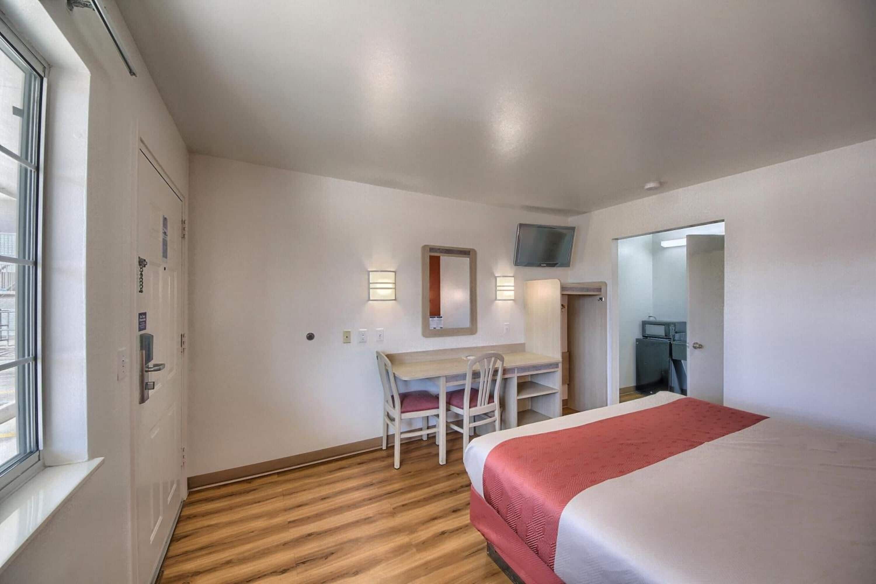Een hotelkamer met een bed, een bureau, twee stoelen, een televisie en een raam.