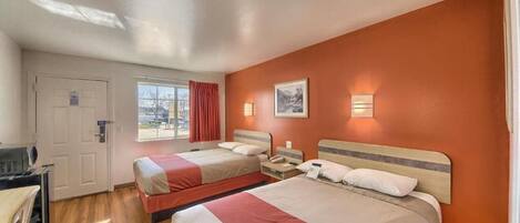 Habitación de hotel con dos camas, un escritorio, una silla, un ventanal con cortinas y una puerta.