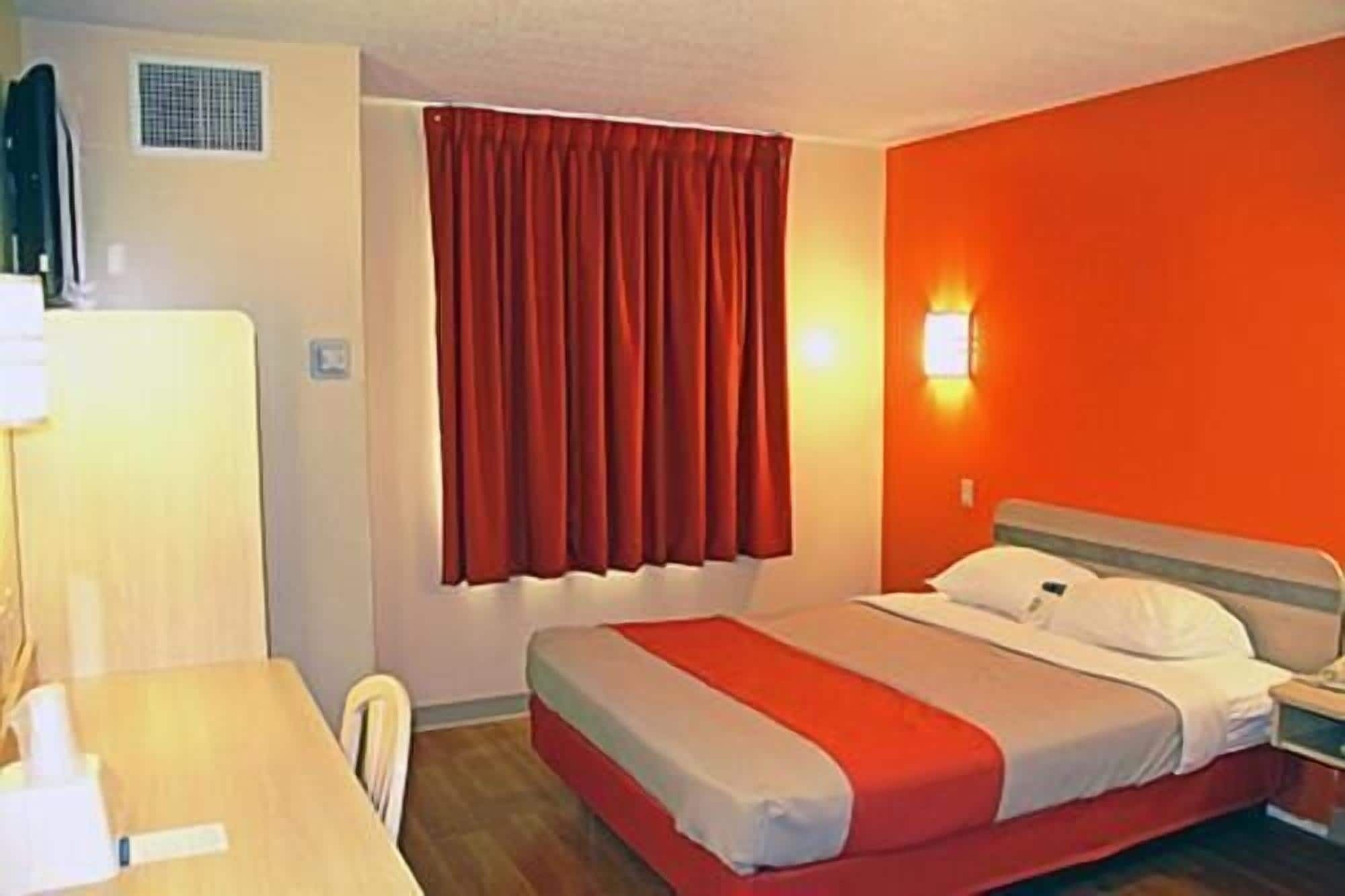 Una habitació d'hotel amb un llit, una taula de treball, una cadira i una finestra amb cortines.