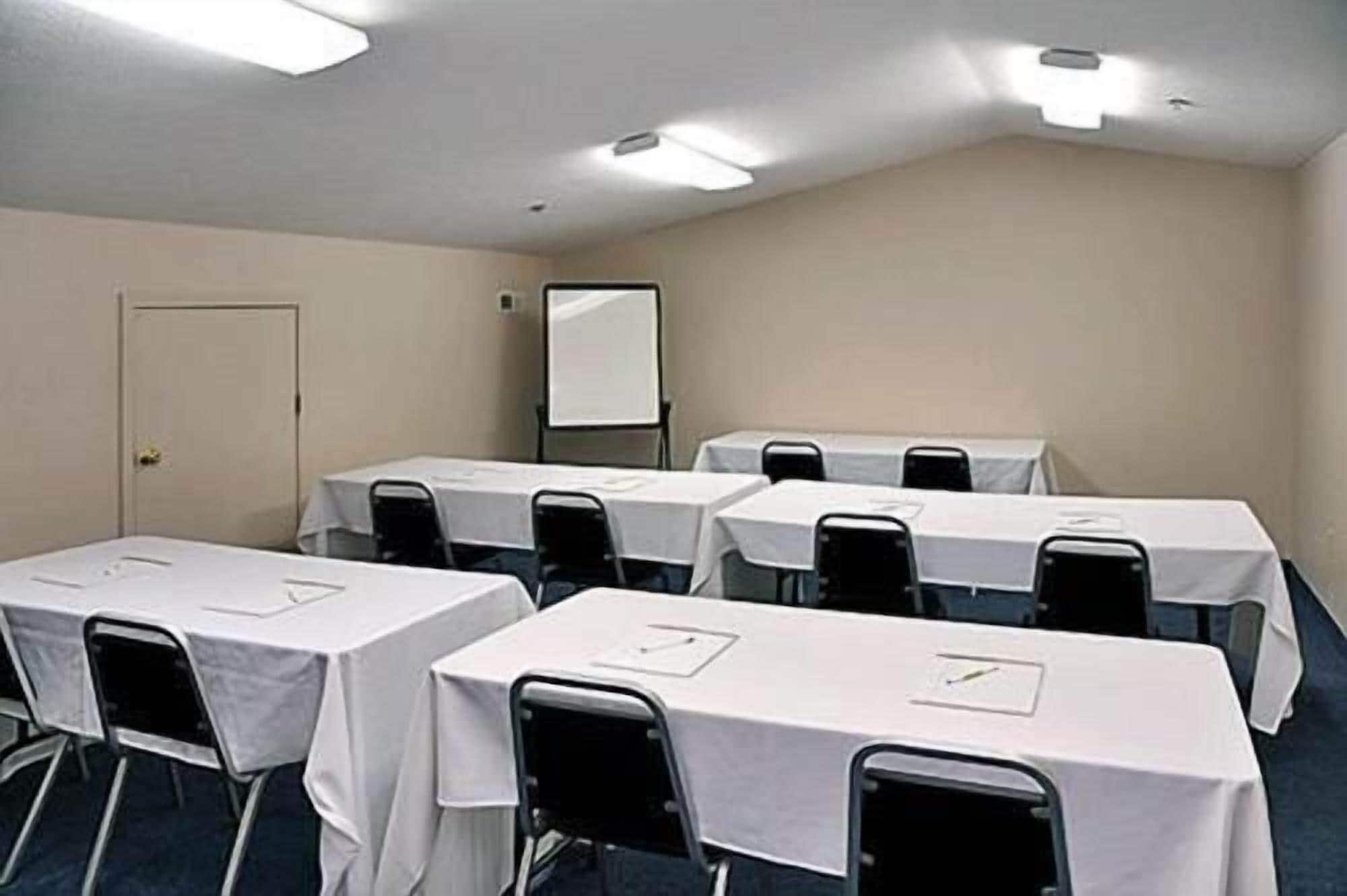 A conference room with tables covered in white tablecloths, black chairs, and a whiteboard on the wall.