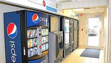A row of Pepsi vending machines in a hallway with a tiled floor and an exit door visible in the background.