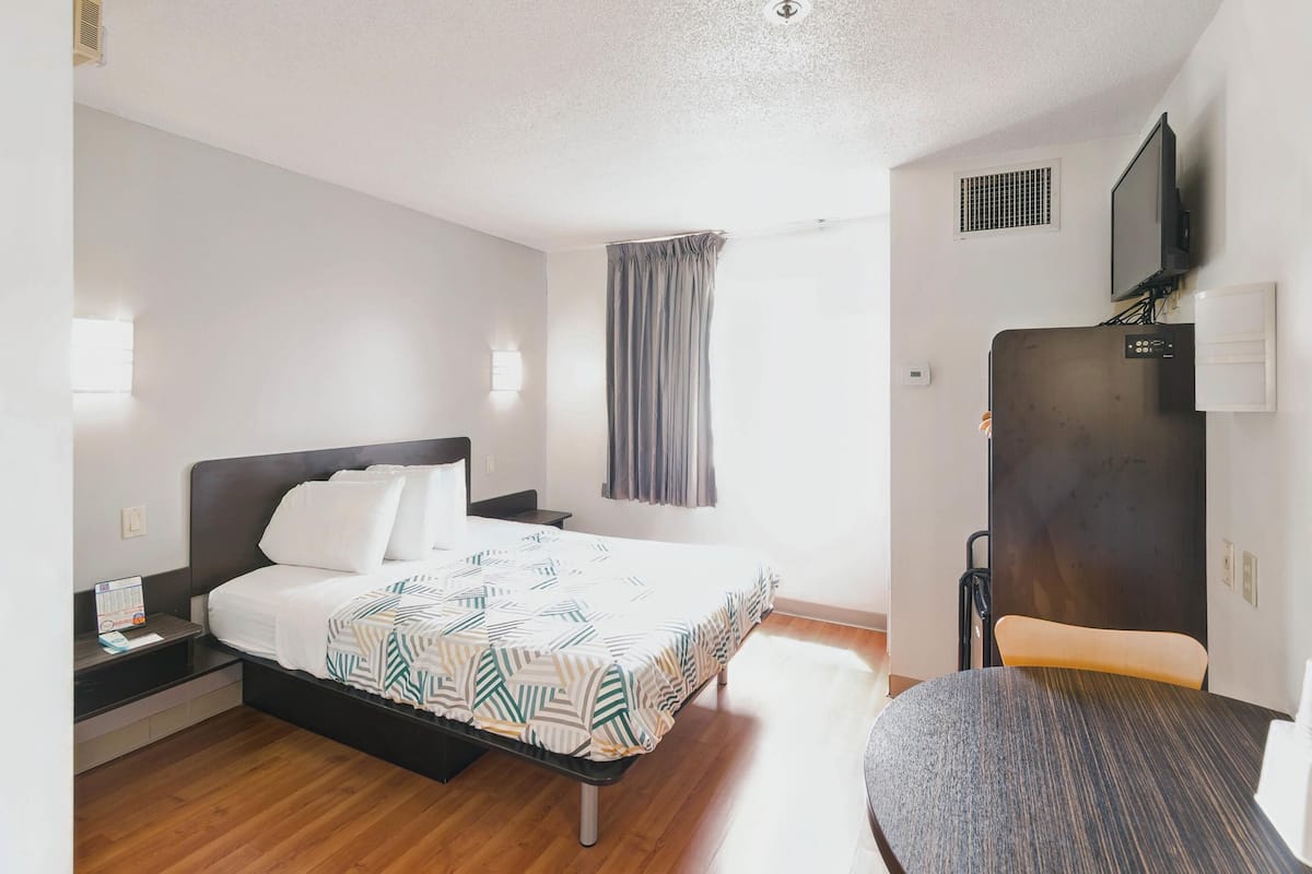 A hotel room with a bed, bedside table, chair, and a TV mounted on the wall.