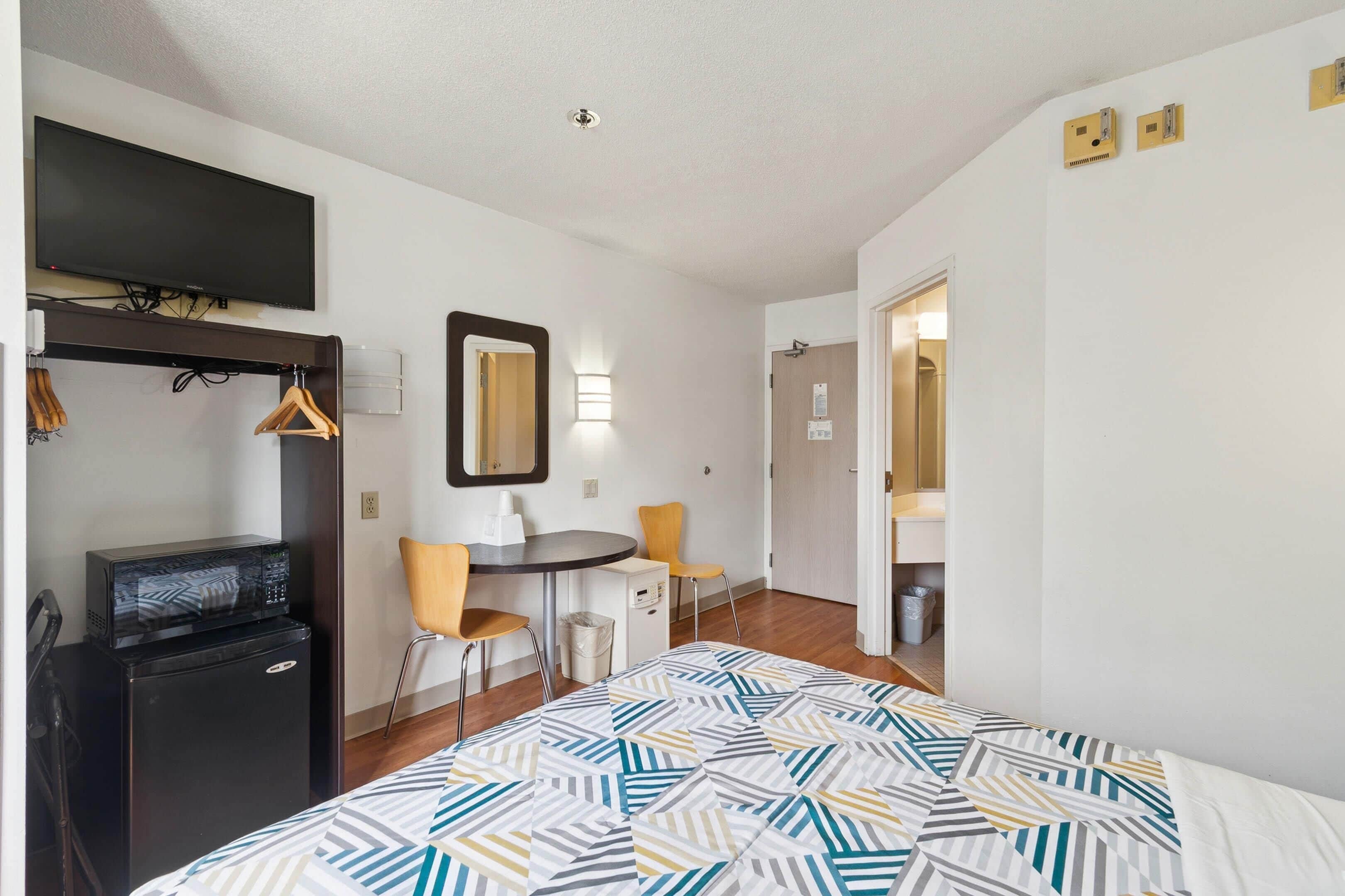 Camera d'albergo con un letto, una scrivania con un computer, un forno a microonde, un piccolo frigorifero, una TV a muro e uno specchio.