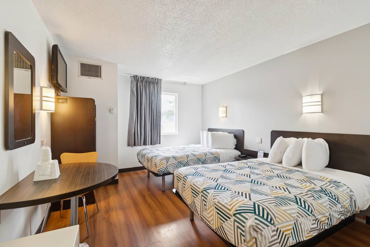 A hotel room with two beds, a desk, a chair, a TV, and a window with curtains.