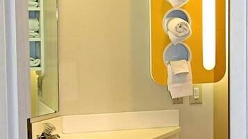 A bathroom with a sink, mirror, towel dispenser, and toilet paper.
