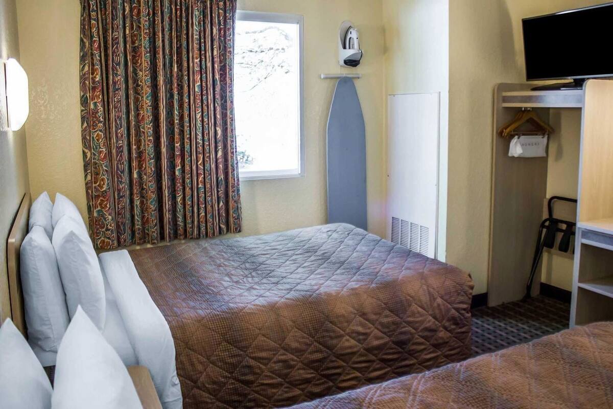A hotel room with a bed, a TV, a wardrobe, and a window with curtains.