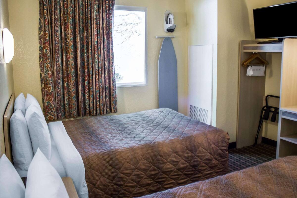 A hotel room with two beds, a wardrobe, a television, and a window with curtains.