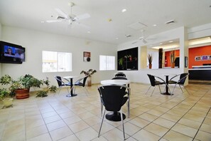A spacious indoor area with multiple tables and chairs, ceiling fans, and potted plants. - Motel 6 Benson, AZ (Benson)