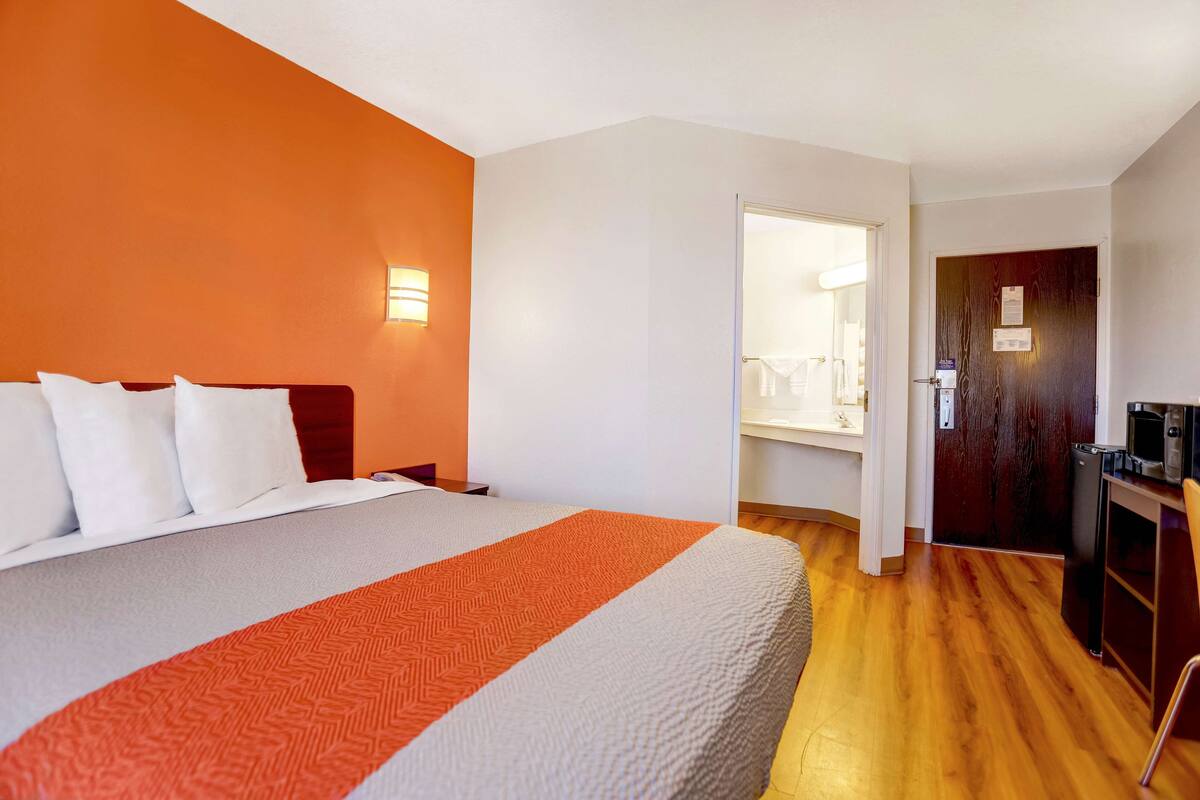 A hotel room with a large bed, a wooden desk, and a bathroom visible through an open door.