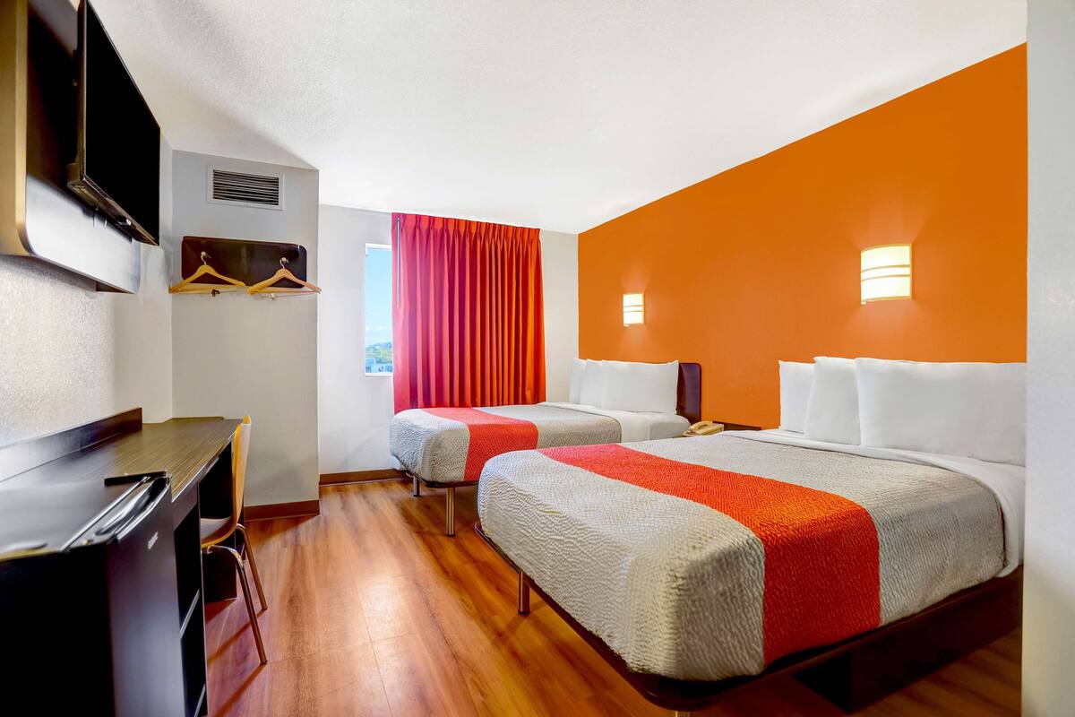 A hotel room with two beds, a desk, and a TV.