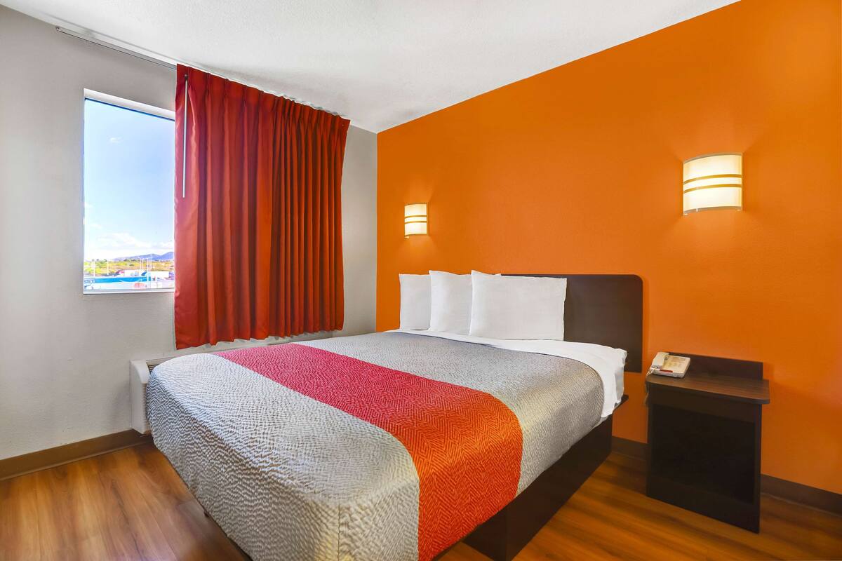 A hotel room with a large bed, red curtains, two wall-mounted lights, and a small bedside table with a phone.
