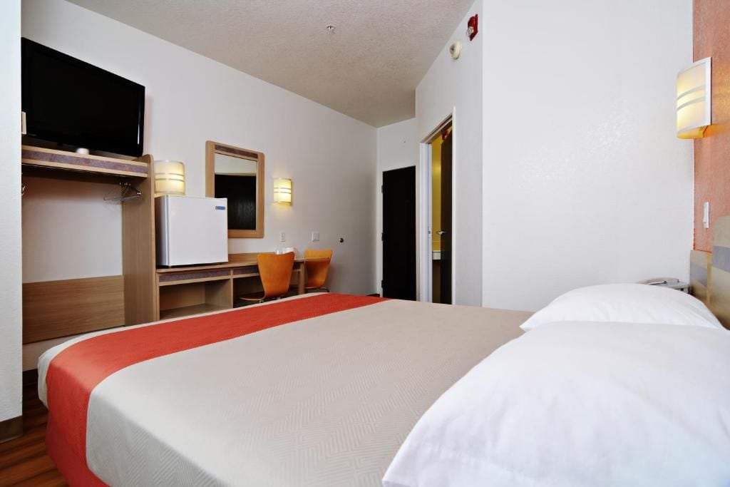Ett hotellrum med en säng, ett skrivbord med en stol, en tv och en spegel.