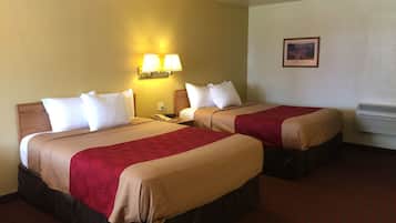 Habitación de hotel con dos camas, cada una con colcha roja y color beige, almohadas blancas y cabeceros de madera. Hay una lámpara de pared sobre las camas y un cuadro en la pared.