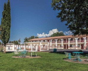 A hotel with a courtyard, outdoor seating, and a large tree. - Rodeway Inn Hurricane - Zion National Park Area (Hurricane)