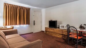 A hotel room with a sofa, a dining table with chairs, a television, a microwave, and a door.