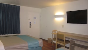 Camera d'albergo con due letti, una scrivania, una sedia, una televisione e un cestino.