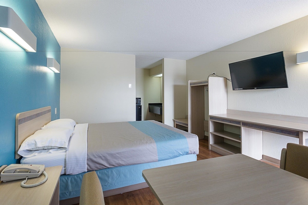 Habitació d'hotel amb llit, taula de nit amb telèfon, escriptori amb televisió de pantalla plana i una cadira.