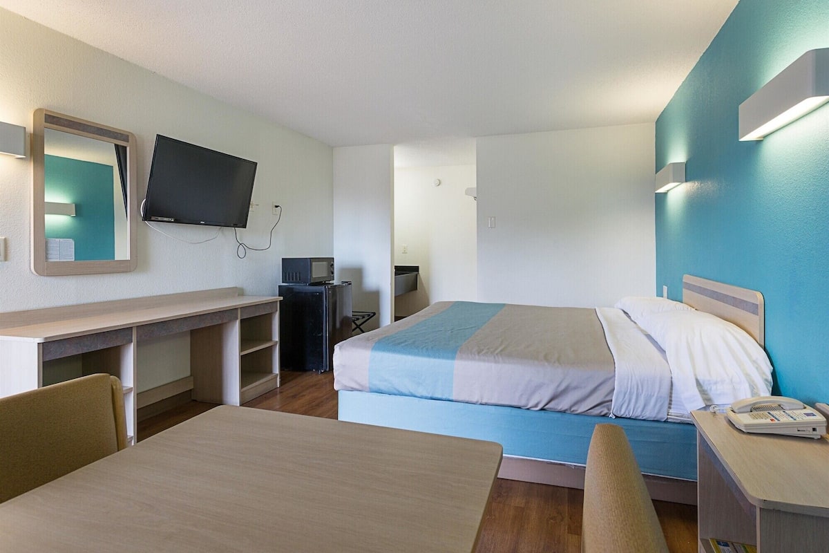 Habitació d'hotel amb llit, escriptori, cadira, televisió i una taula petita.