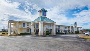 Un motel con un edificio centrale e due ali, caratterizzato da un tetto blu e un cartello con un grande numero '6'.