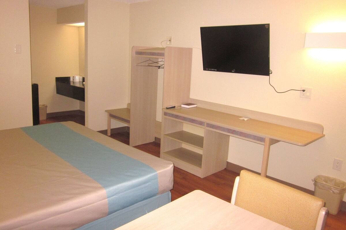 Habitació d'hotel amb un llit, una taula de nit, una cadira, un televisor i un armari.