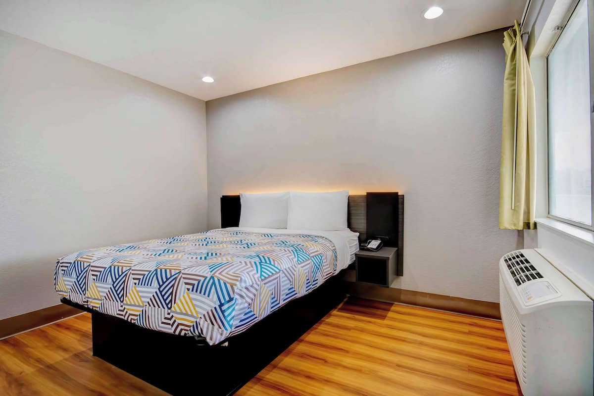 Ein modernes Hotelzimmer mit einem ordentlich bezogenen Bett, einem Nachttisch mit Telefon und einer Wandklimaanlage.