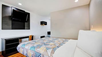 Une chambre d’hôtel moderne équipée d’un lit, d’un bureau et d’un téléviseur fixé au mur.