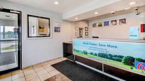 A reception area with a digital screen displaying a booking message, a reception desk, and a security camera. - Motel 6 Port Allen, LA - Baton Rouge (Port Allen)