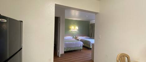Una habitación de hotel compacta con kitchenette, dos camas, una pequeña mesa de comedor y piso de madera.