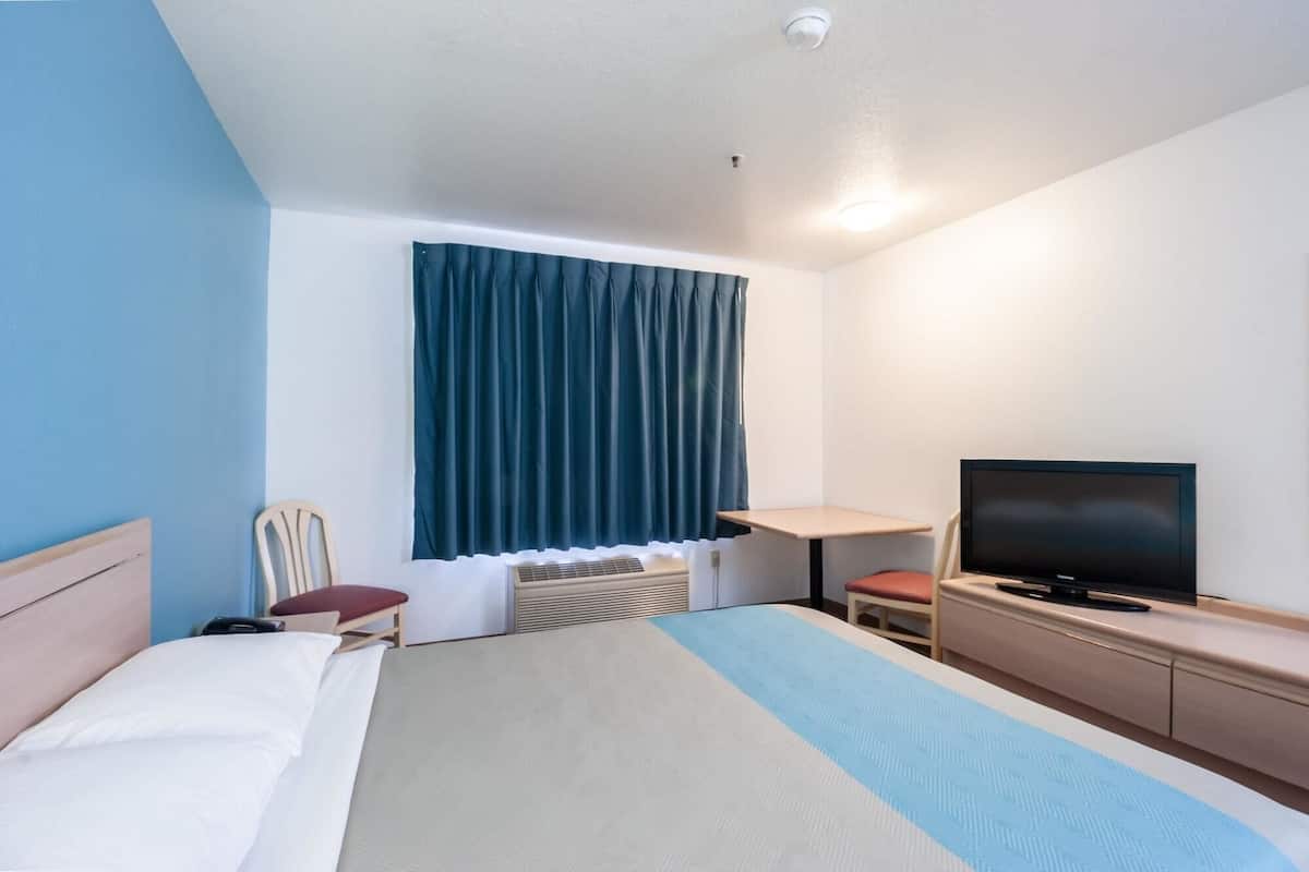 A hotel room with a bed, a desk, a television, and a window with curtains.