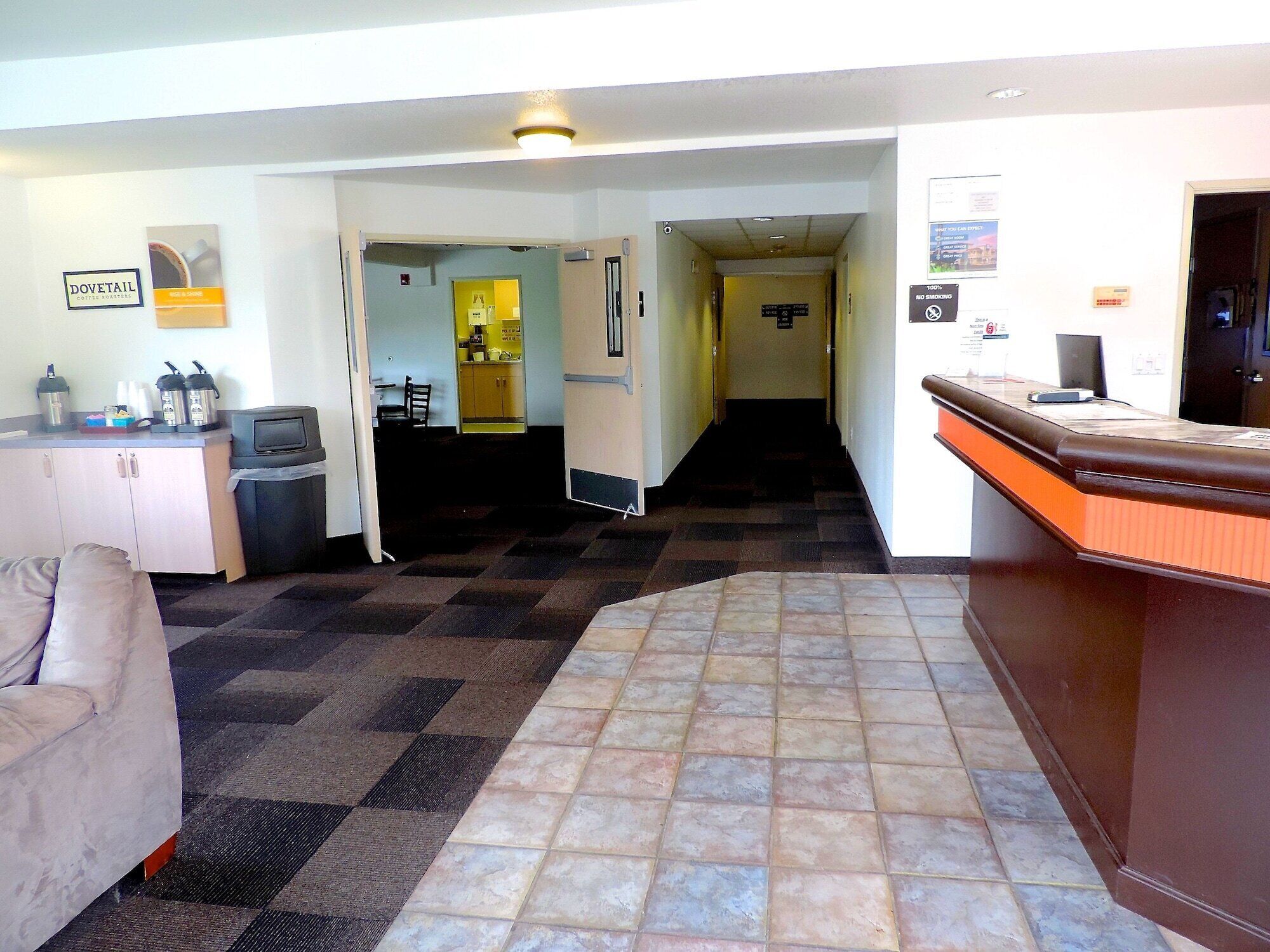 Un hall de hotel con una recepción, una kitchenette, un área de descanso y un pasillo que lleva a otras habitaciones.