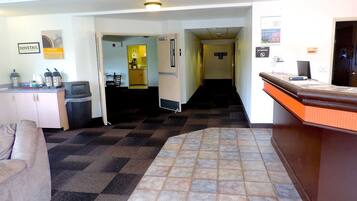 Un hall de hotel con una recepción, una kitchenette, un área de descanso y un pasillo que lleva a otras habitaciones.
