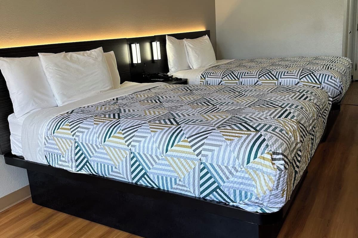 A double bed with a geometric patterned bedspread, a black headboard with integrated lighting, and a wooden floor.