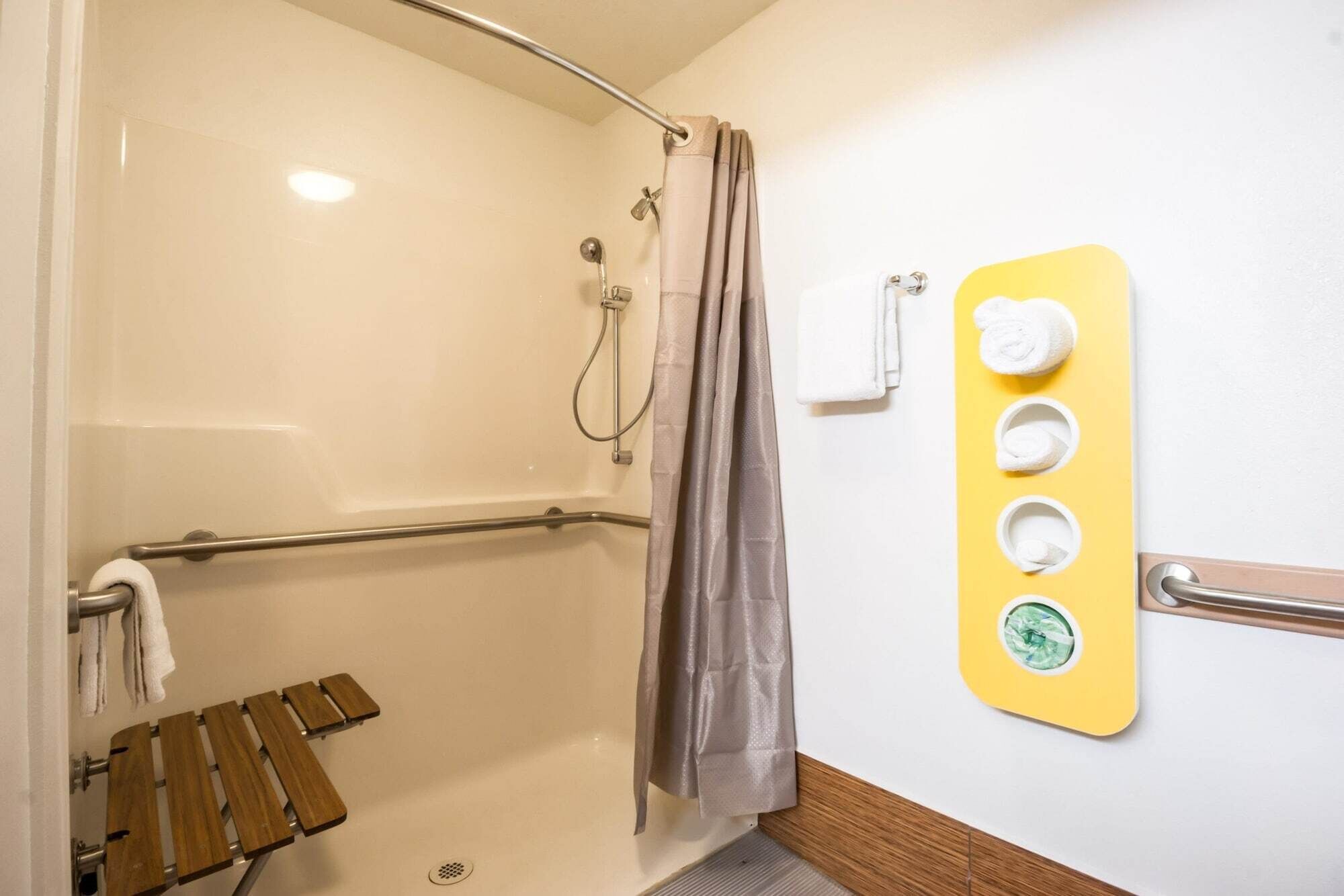 A shower area with a grab bar, a wooden bench, a towel rack, and a soap dish.