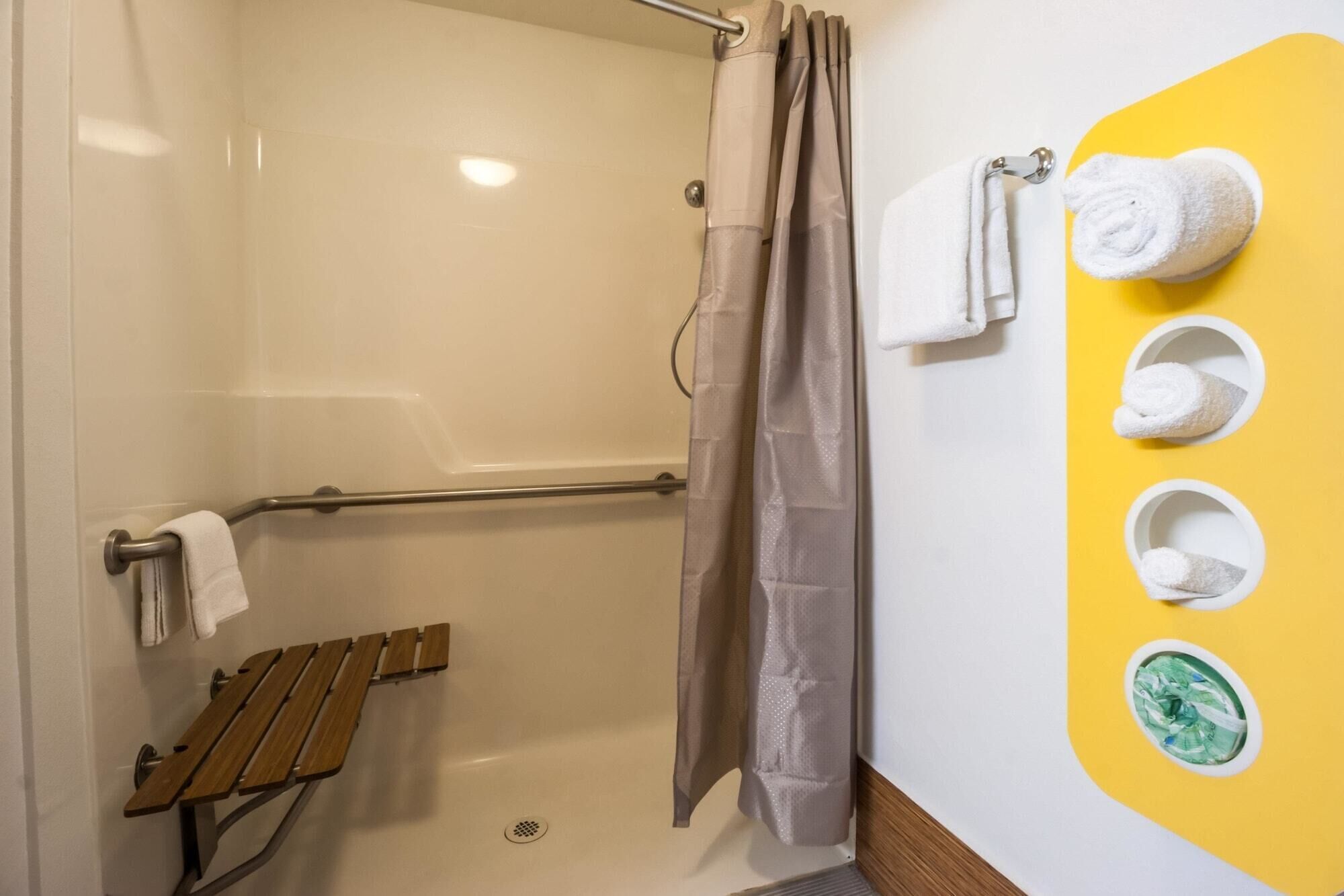 Douchegedeelte met een bankje, een handdoekhouder en een gele wand met handdoekhouders.