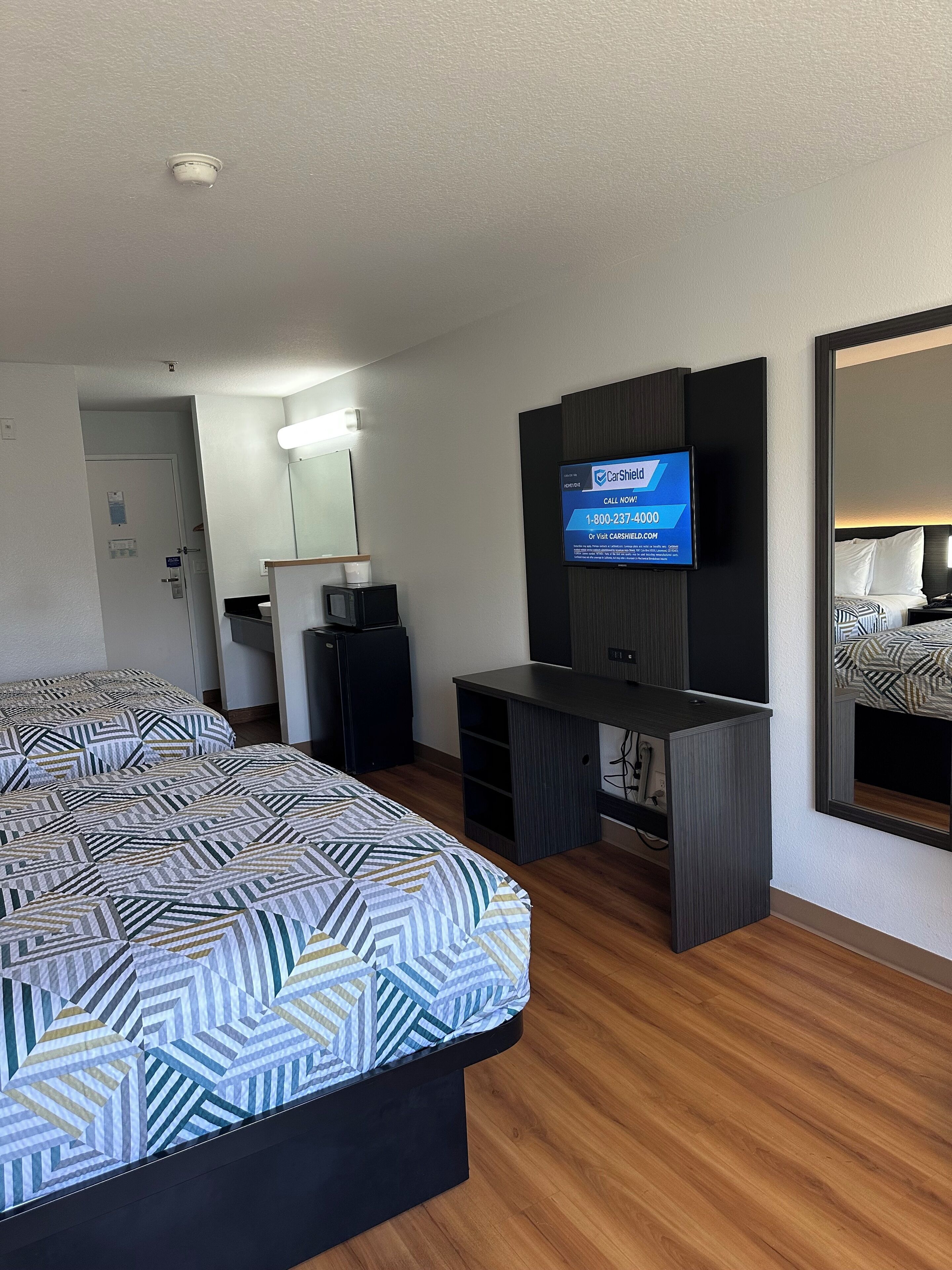 A hotel room with a bed, a desk, a TV, and a mirror.